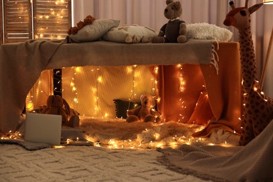 Beautiful play tent decorated with festive lights and toys at home