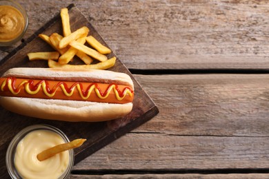 Delicious hot dog, sauces and French fries on wooden table, top view. Space for text