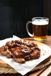 Tasty chicken wings and mug of beer on wooden table, space for text. Delicious snack