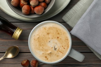 Photo of Mug of delicious coffee with hazelnut syrup on wooden table, flat lay