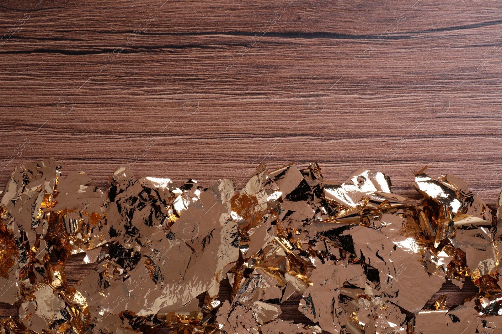 Photo of Many pieces of edible gold leaf on wooden table, top view. Space for text