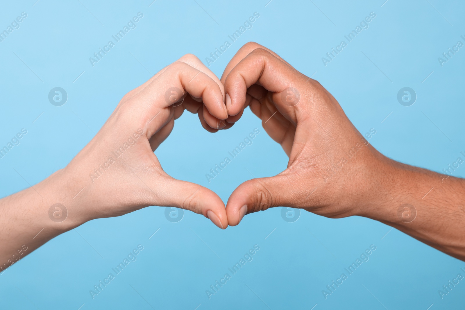 Photo of International relationships. People making heart with hands on light blue background, closeup