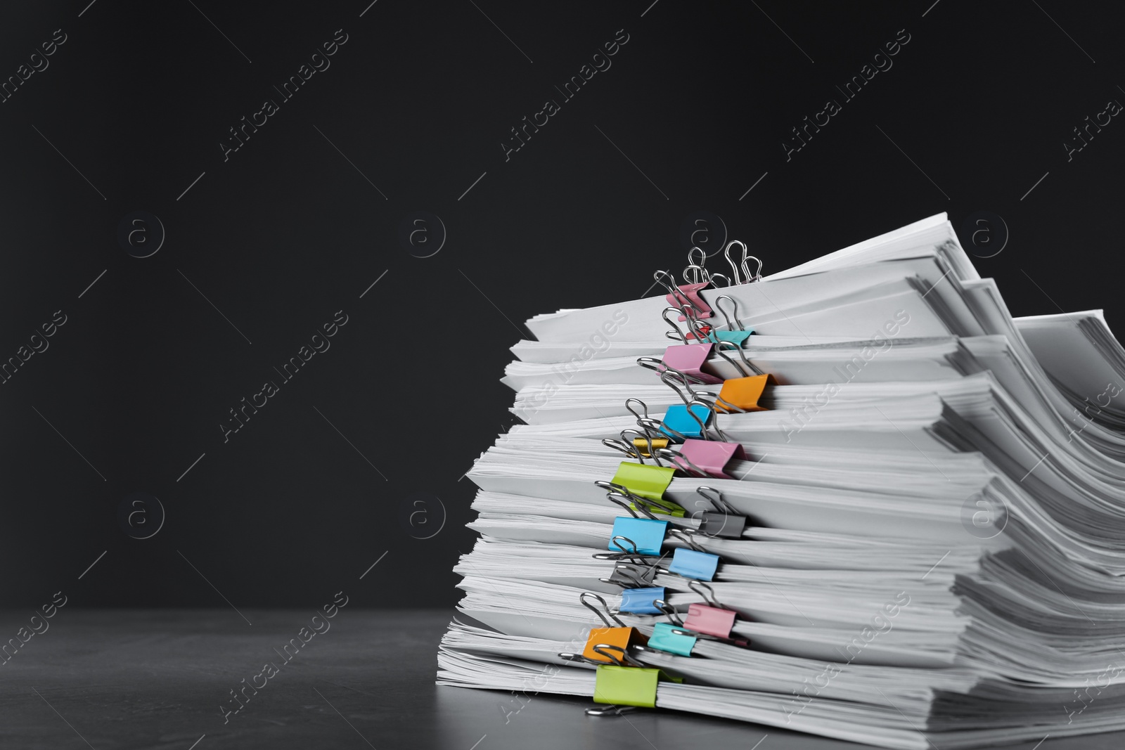 Photo of Stack of documents with binder clips on grey stone table against black background, space for text