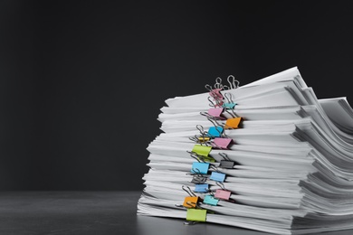Stack of documents with binder clips on grey stone table against black background, space for text