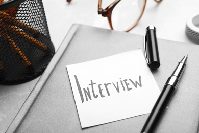 Photo of Reminder note about job interview and stationery on table, closeup