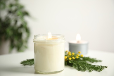 Beautiful candle with wooden wick and flowers on white table