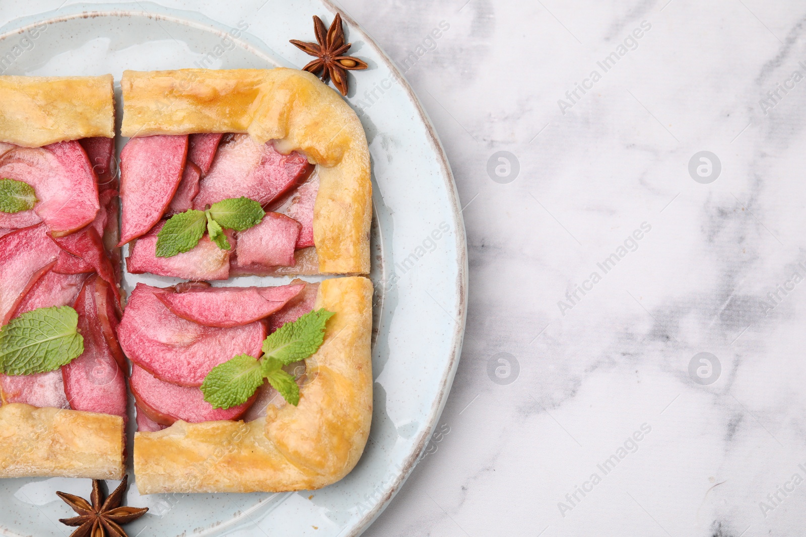 Photo of Delicious apple galette with mint and star anise on white marble table, top view. Space for text