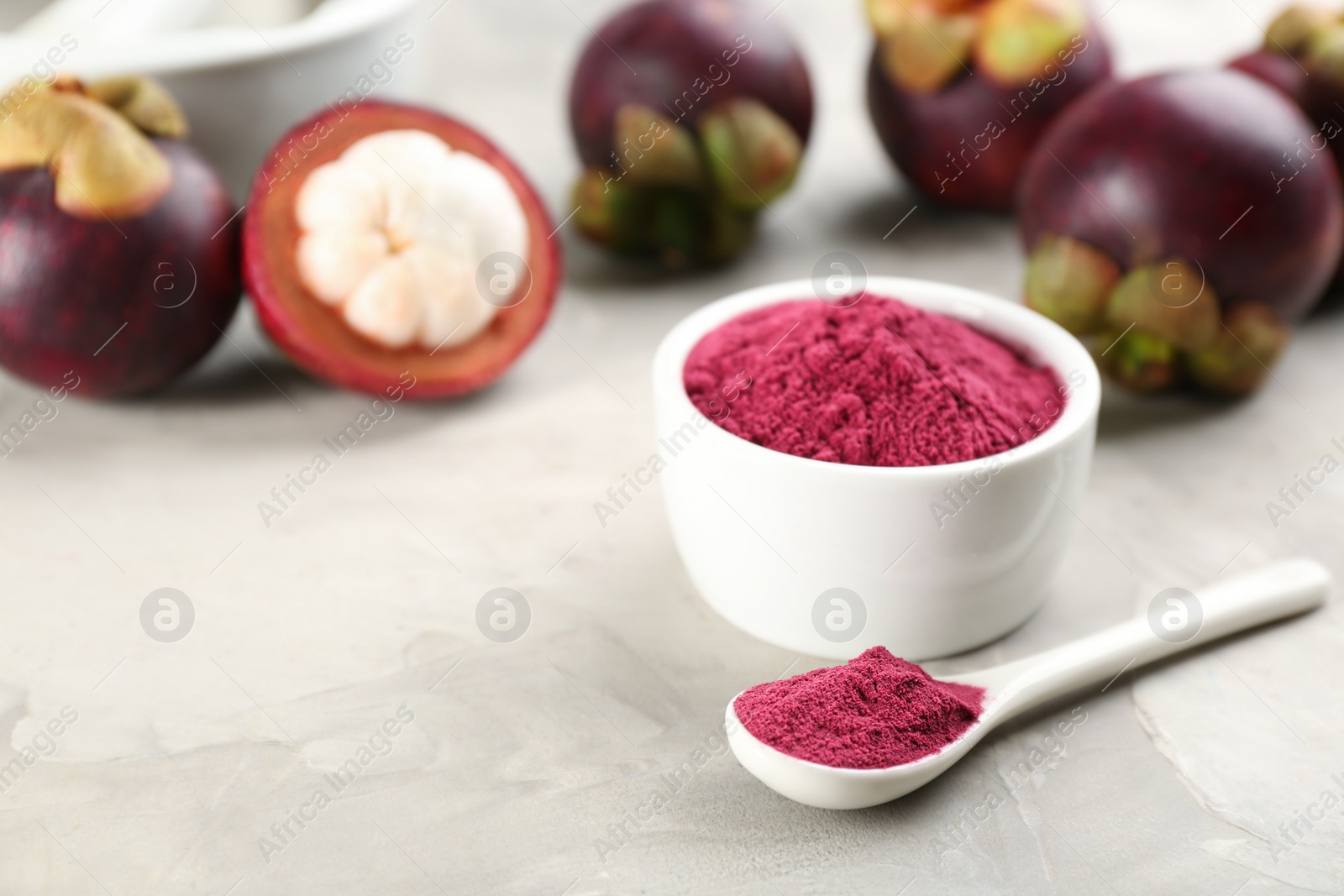 Photo of Purple mangosteen powder and fruits on light grey table