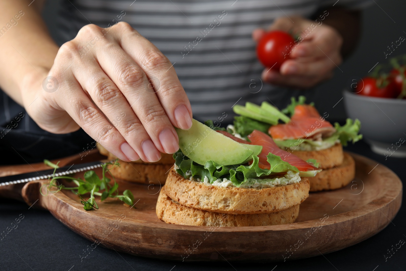 Photo of Woman adding avocado onto tasty rusks with salmon and cream cheese at black table, closeup