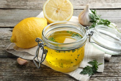 Photo of Jar with lemon sauce and ingredients on wooden table. Delicious salad dressing