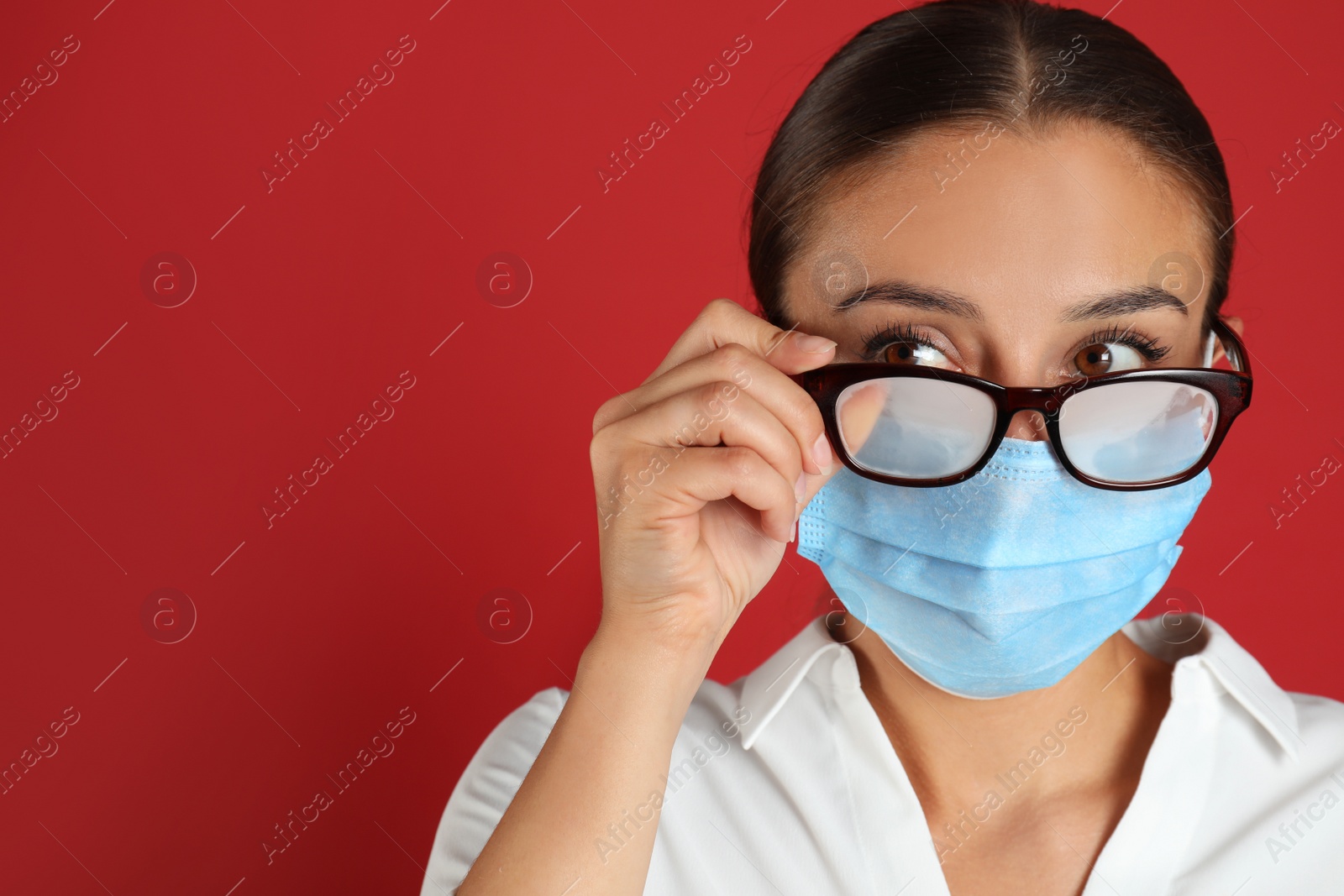 Photo of Woman wiping foggy glasses caused by wearing medical mask on red background. Space for text