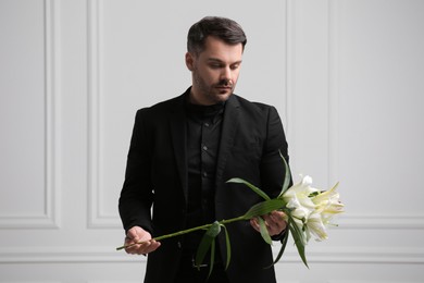 Photo of Sad man with lily flowers near white wall. Funeral ceremony