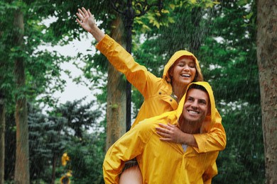 Photo of Lovely couple with raincoats having fun under rain in park