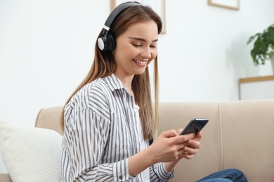Photo of Young woman with headphones and smartphone on sofa at home