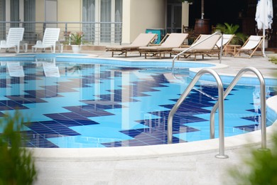 Outdoor swimming pool with handrails and many empty sunbeds at resort