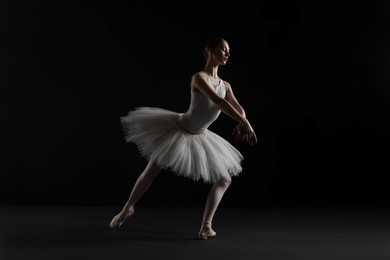 Photo of Young ballerina practicing dance moves on black background