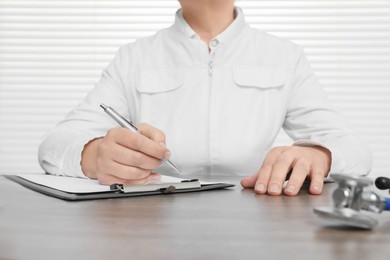 Photo of Professional doctor writing in clipboard at wooden table, closeup