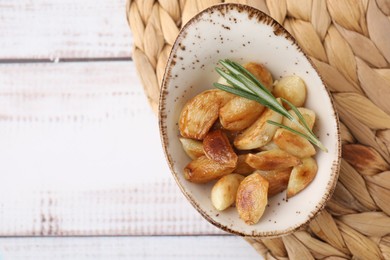 Photo of Fried garlic cloves and rosemary on white wooden table, top view. Space for text