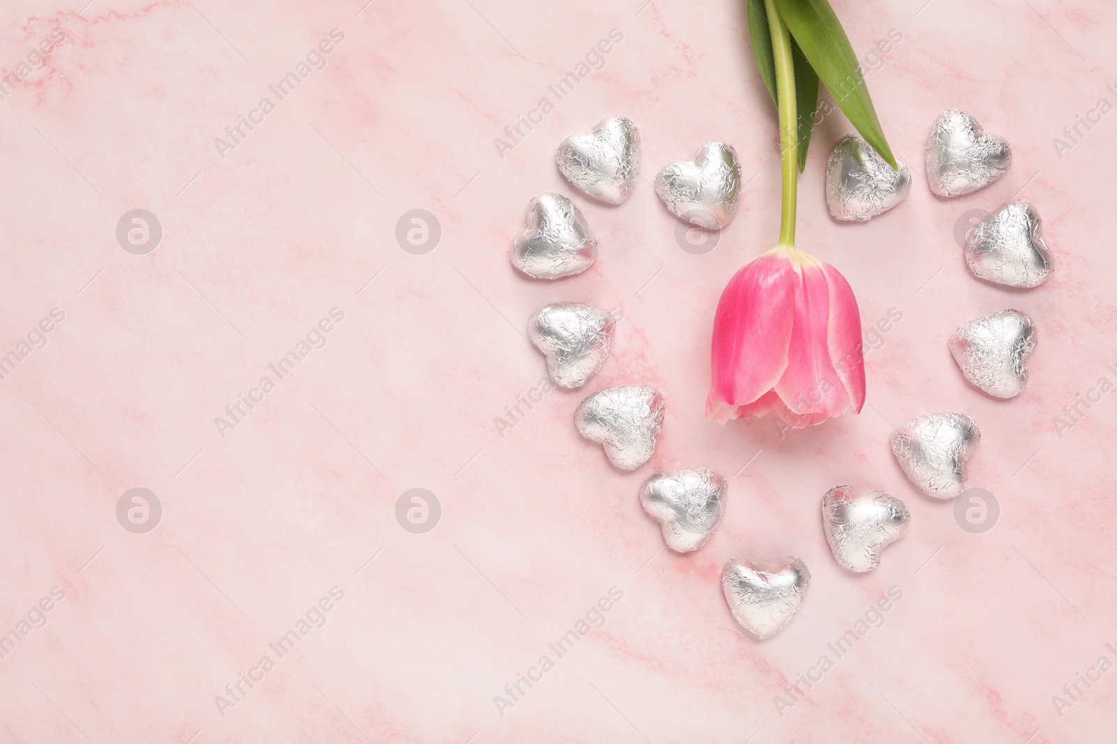 Photo of Heart made with delicious chocolate candies and beautiful tulip on pink table, flat lay. Space for text