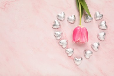 Photo of Heart made with delicious chocolate candies and beautiful tulip on pink table, flat lay. Space for text