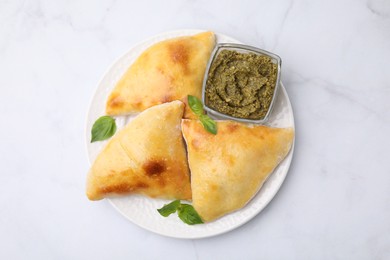 Photo of Delicious samosas with basil and pesto sauce on white marble table, top view