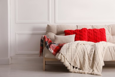 Photo of Different warm plaids and pillows on sofa in living room