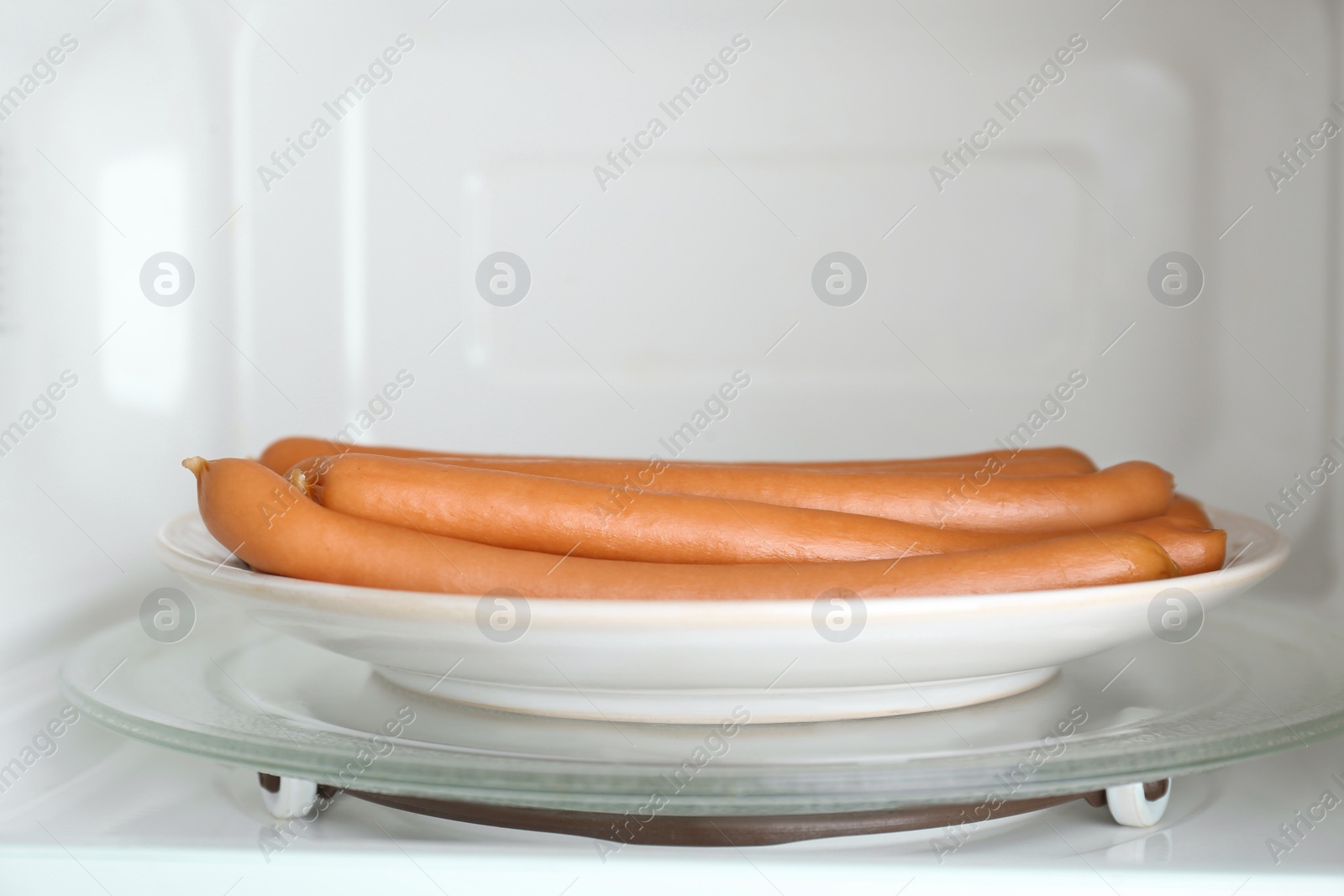 Photo of Tasty sausages on plate in microwave oven. Meat product