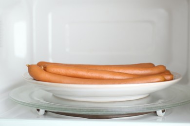 Photo of Tasty sausages on plate in microwave oven. Meat product