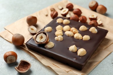 Photo of Delicious chocolate bar and hazelnuts on light table