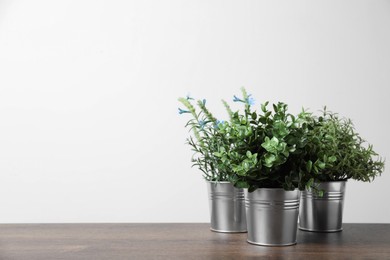 Different artificial potted herbs on wooden table against white background, space for text