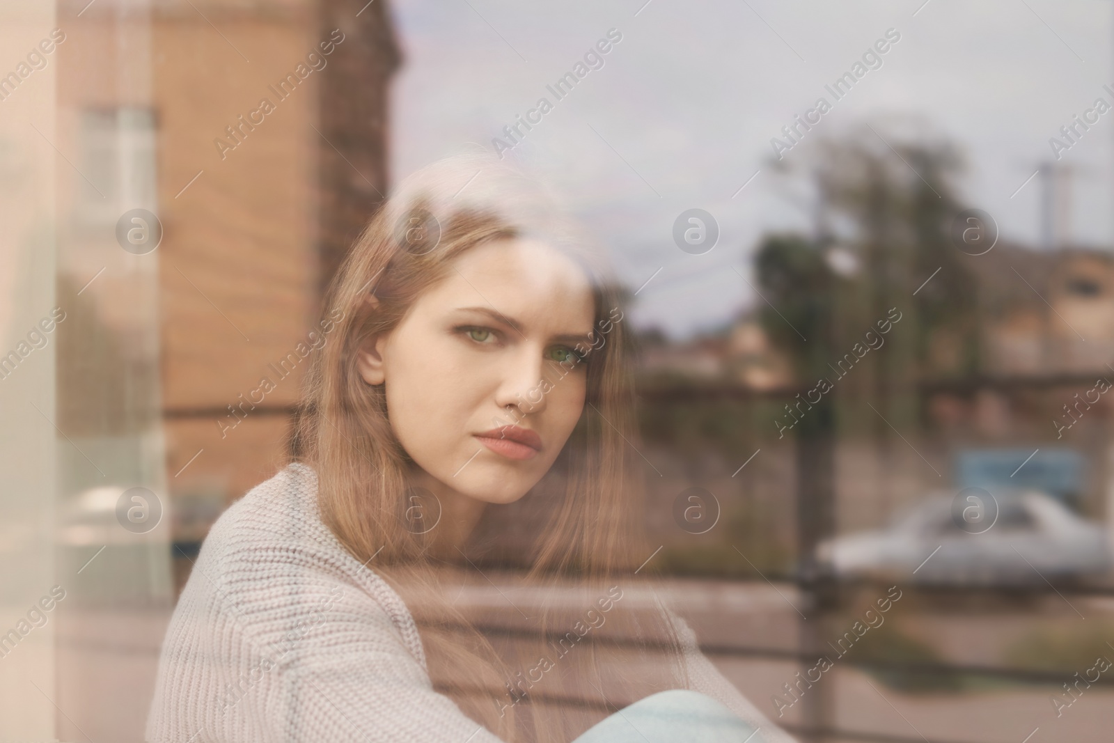 Photo of Depressed young woman near window, view from outside