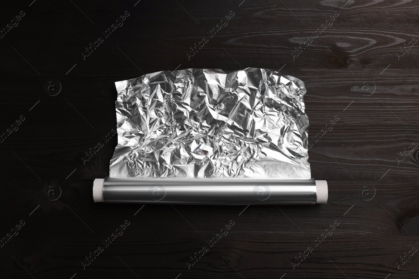 Photo of Roll of aluminum foil on dark wooden table, top view