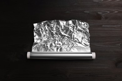 Photo of Roll of aluminum foil on dark wooden table, top view