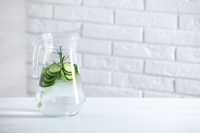 Photo of Refreshing cucumber water with rosemary in jug on white table against brick wall. Space for text