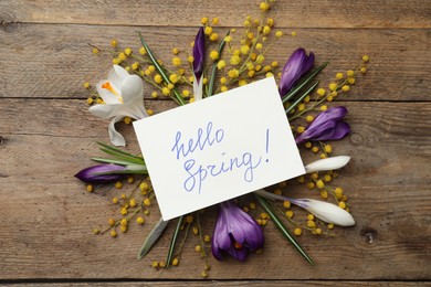 Card with words HELLO SPRING and fresh flowers on wooden table, flat lay