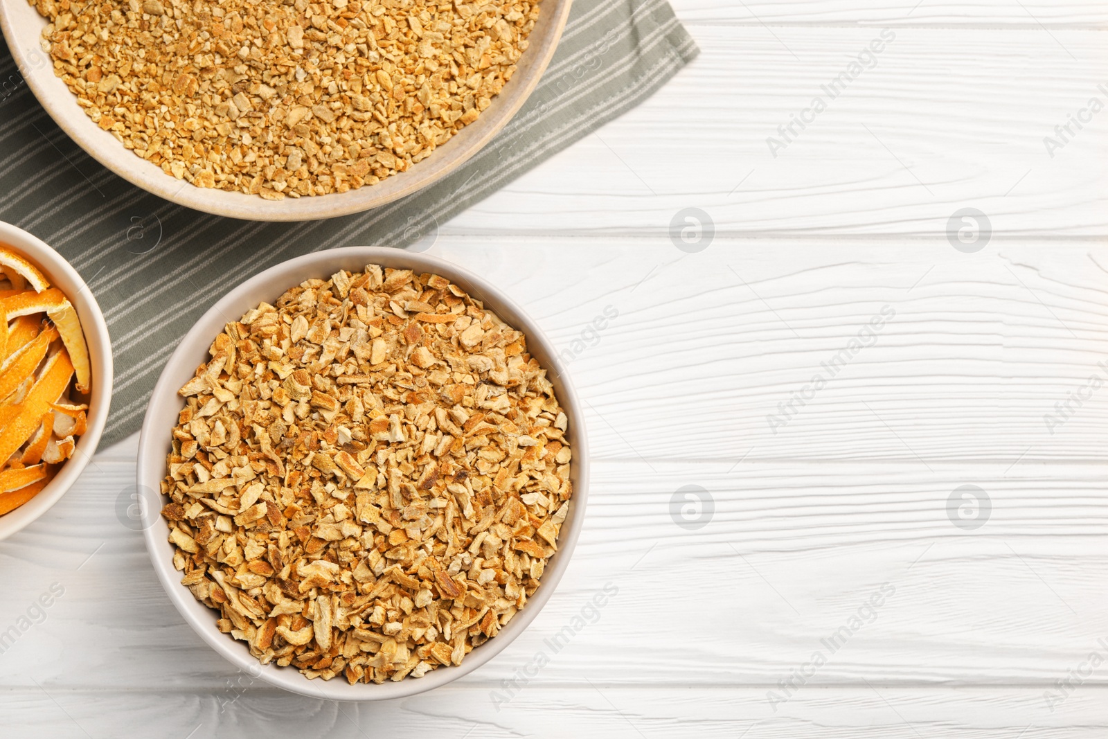 Photo of Bowls with dried orange seasoning zest and peel on white wooden table, flat lay. Space for text