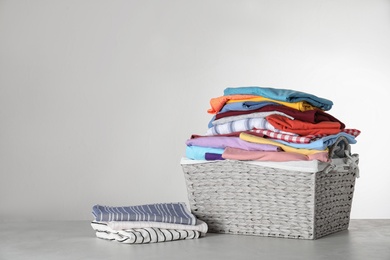 Photo of Wicker laundry basket with clean clothes on table against light background. Space for text