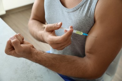 Photo of Athletic man injecting himself at table indoors, closeup. Doping concept