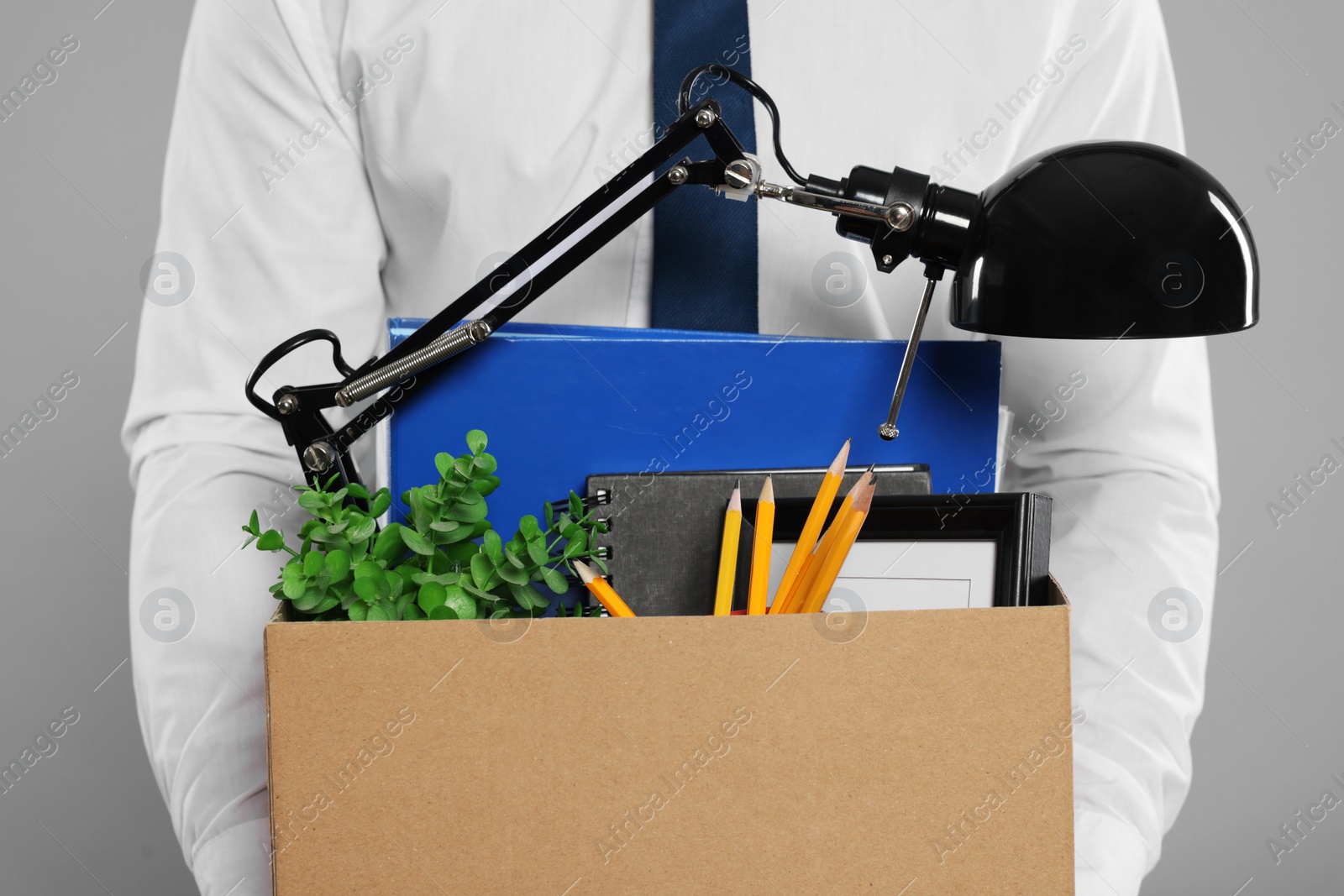 Photo of Unemployed man with box of personal office belongings on light grey background, closeup