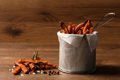 Photo of Frying basket with sweet potato fries on wooden table. Space for text