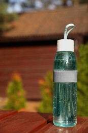Glass bottle of fresh water on wooden table outdoors