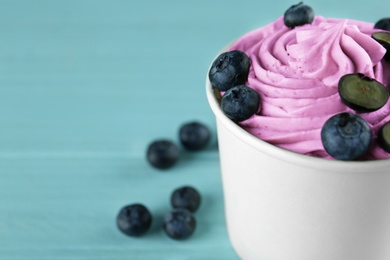 Cup with tasty frozen yogurt and blueberries on blue wooden table, closeup. Space for text