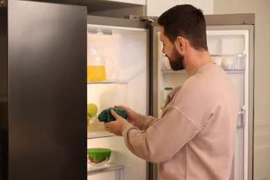 Man putting bowl covered with beeswax food wrap into refrigerator indoors