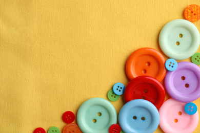 Many bright sewing buttons on yellow fabric, flat lay. Space for text