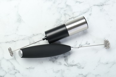 Black milk frother wands on white marble table, top view