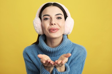 Photo of Beautiful young woman wearing earmuffs on yellow background