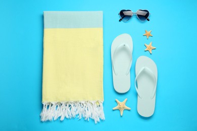 Beach towel, flip flops and sunglasses on light blue background, flat lay