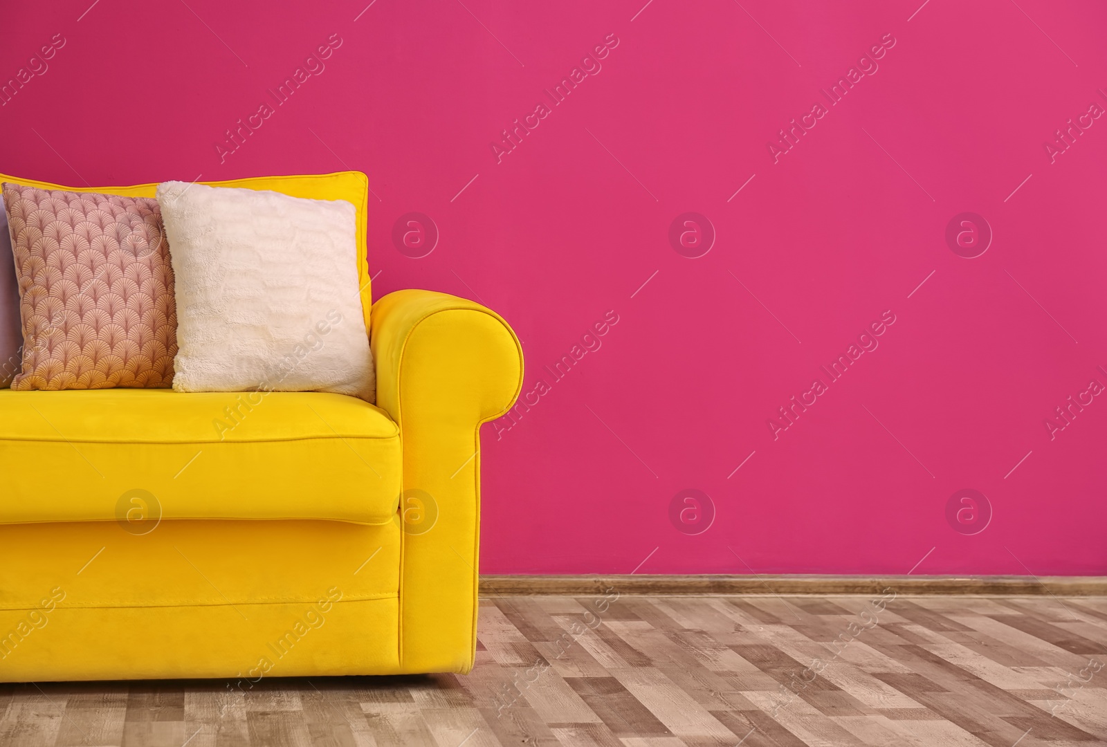 Photo of Sofa with different pillows near color wall in room