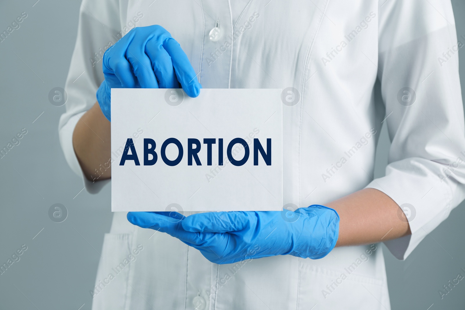 Image of Doctor holding paper card with word Abortion on light grey background, closeup