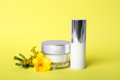 Photo of Luxury face cream, serum and flowers on yellow background